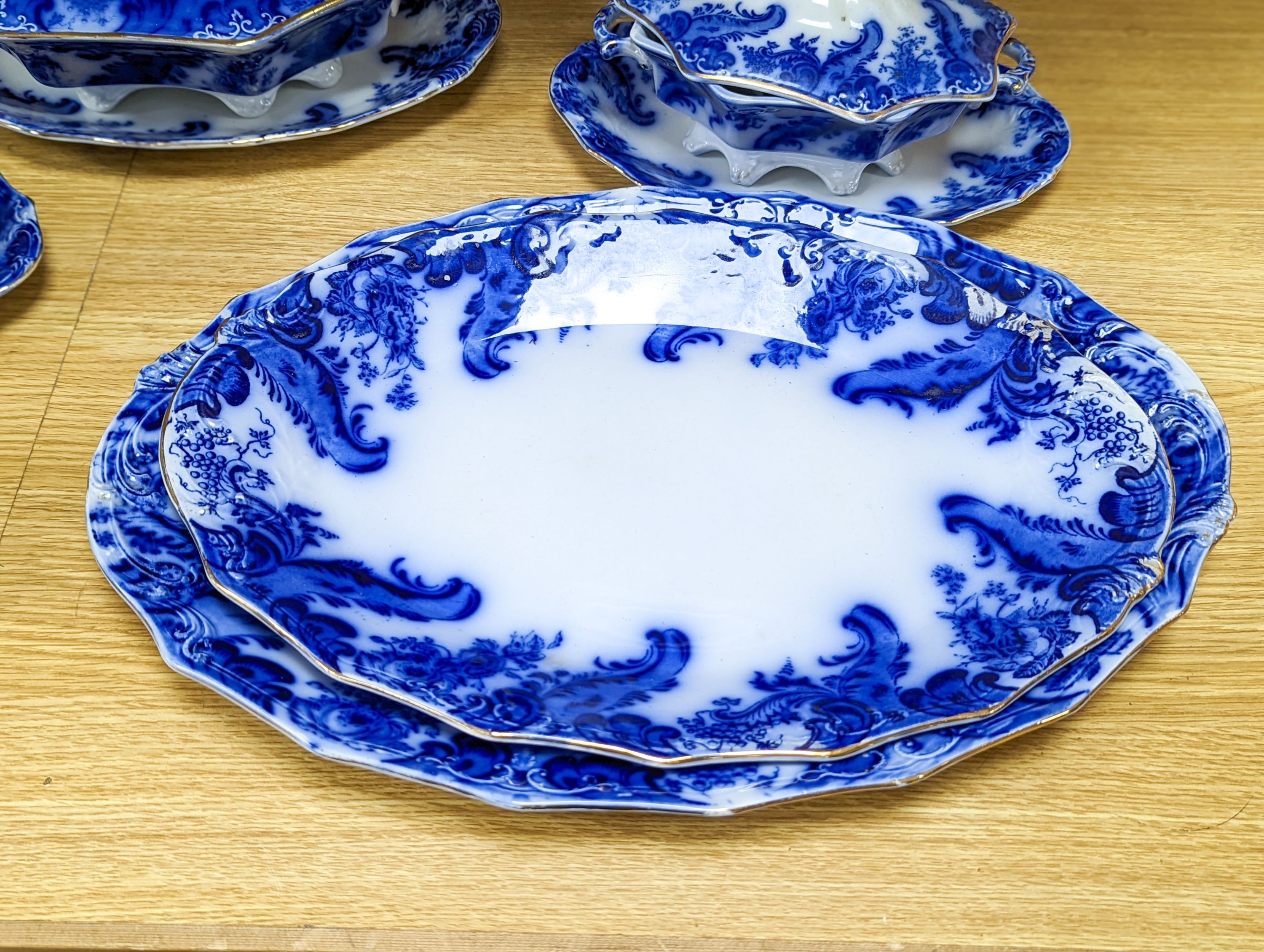 A W. H. Grindley Argyle pattern flow blue dinner service, c.1900 mostly for 12 place settings, two sauce tureens, covers and stands, two vegetable tureens and covers, two gravy boats, and six graduated meat dishes